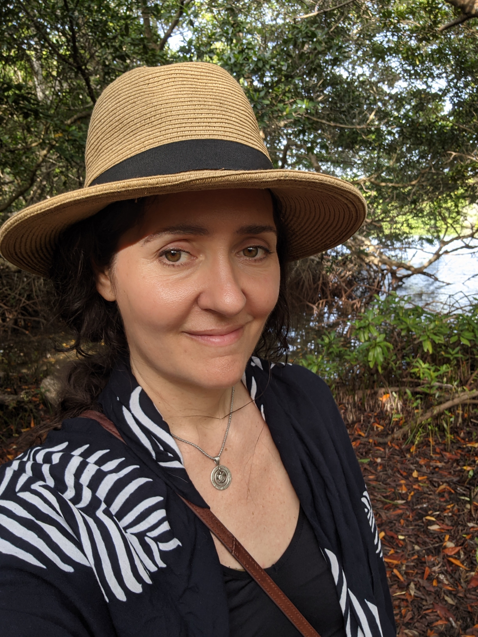 Lori Esposito Lori Esposito smiling outside, with trees behind her. She is wearing a straw hat with a wide brim.