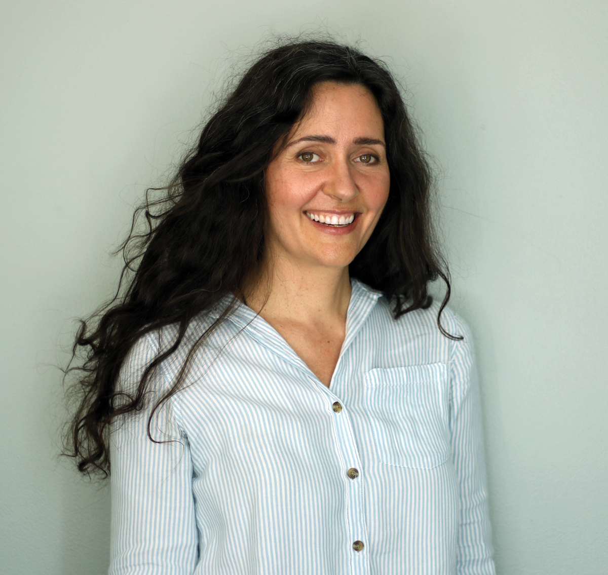 A smiling woman with long brown hair and a white button-down shirt.